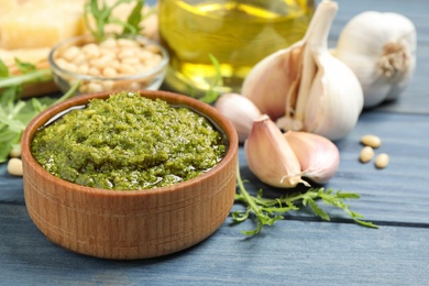 Bowl of tasty arugula pesto and ingredients on blue wooden table