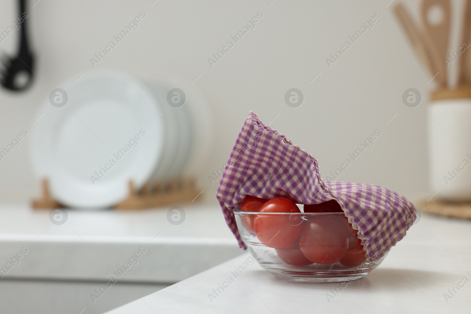 Photo of Tomatoes in bowl covered with beeswax food wrap on white table indoors, space for text