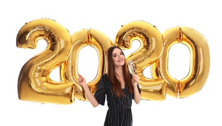 Happy young woman with glass of champagne near golden 2020 balloons on white background. New Year celebration