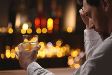 Photo of Man with glass of whiskey against blurred lights, closeup