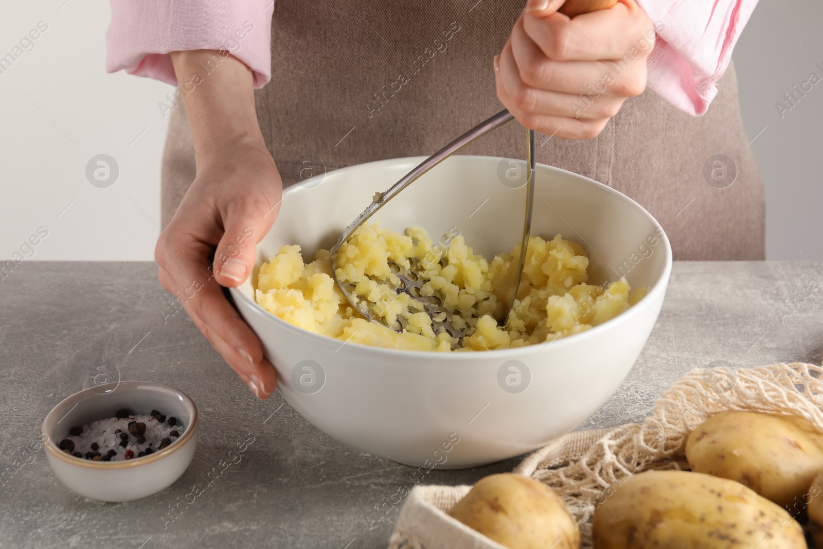 Photo of Woman making mashed potato at light grey table, closeup