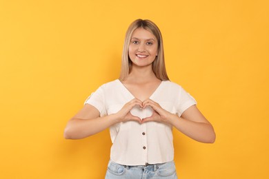 Photo of Happy volunteer making heart with her hands on orange background