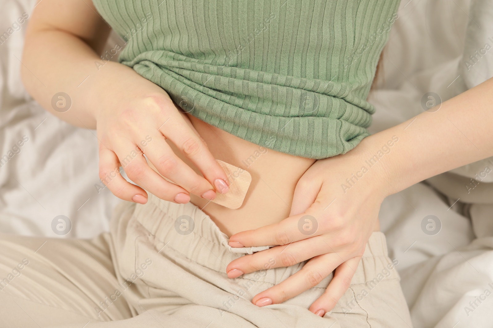 Photo of Woman applying contraceptive patch onto her belly on bed, closeup