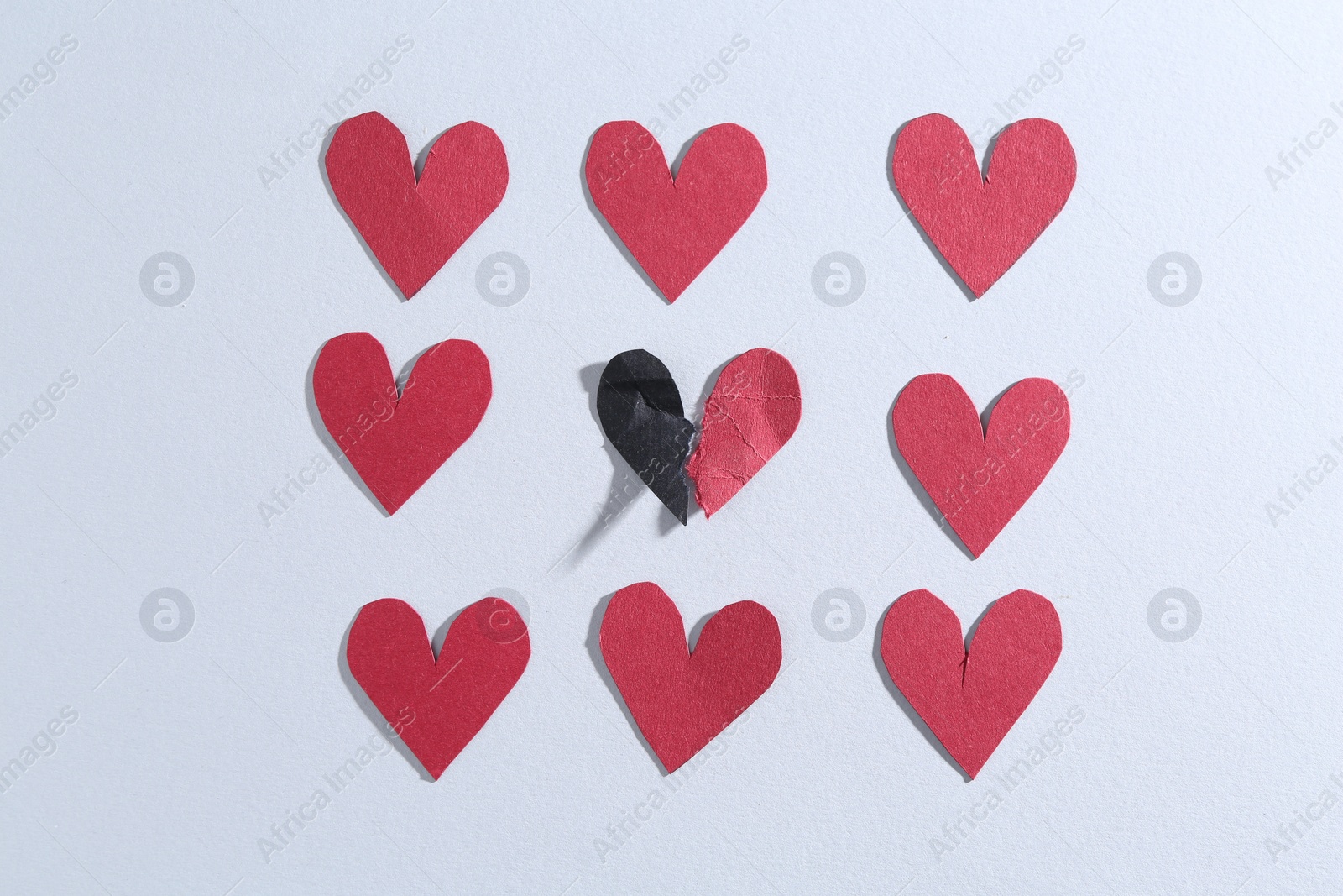 Photo of Halves of torn paper heart and red decorative hearts on gray background, flat lay. Breakup concept