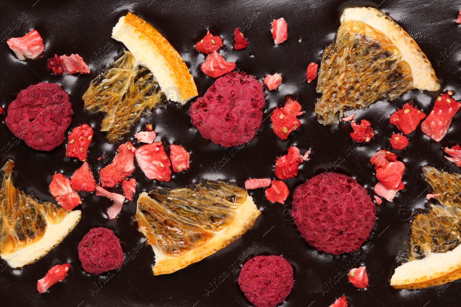 Photo of Chocolate bar with freeze dried oranges and berries as background, closeup