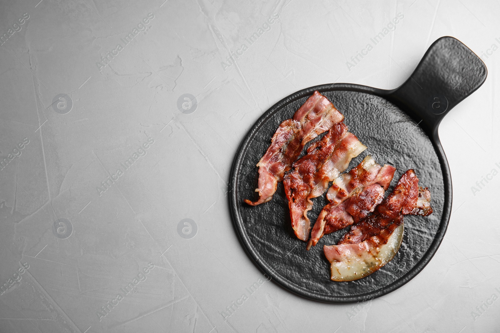 Photo of Slices of tasty fried bacon on grey table, top view. Space for text