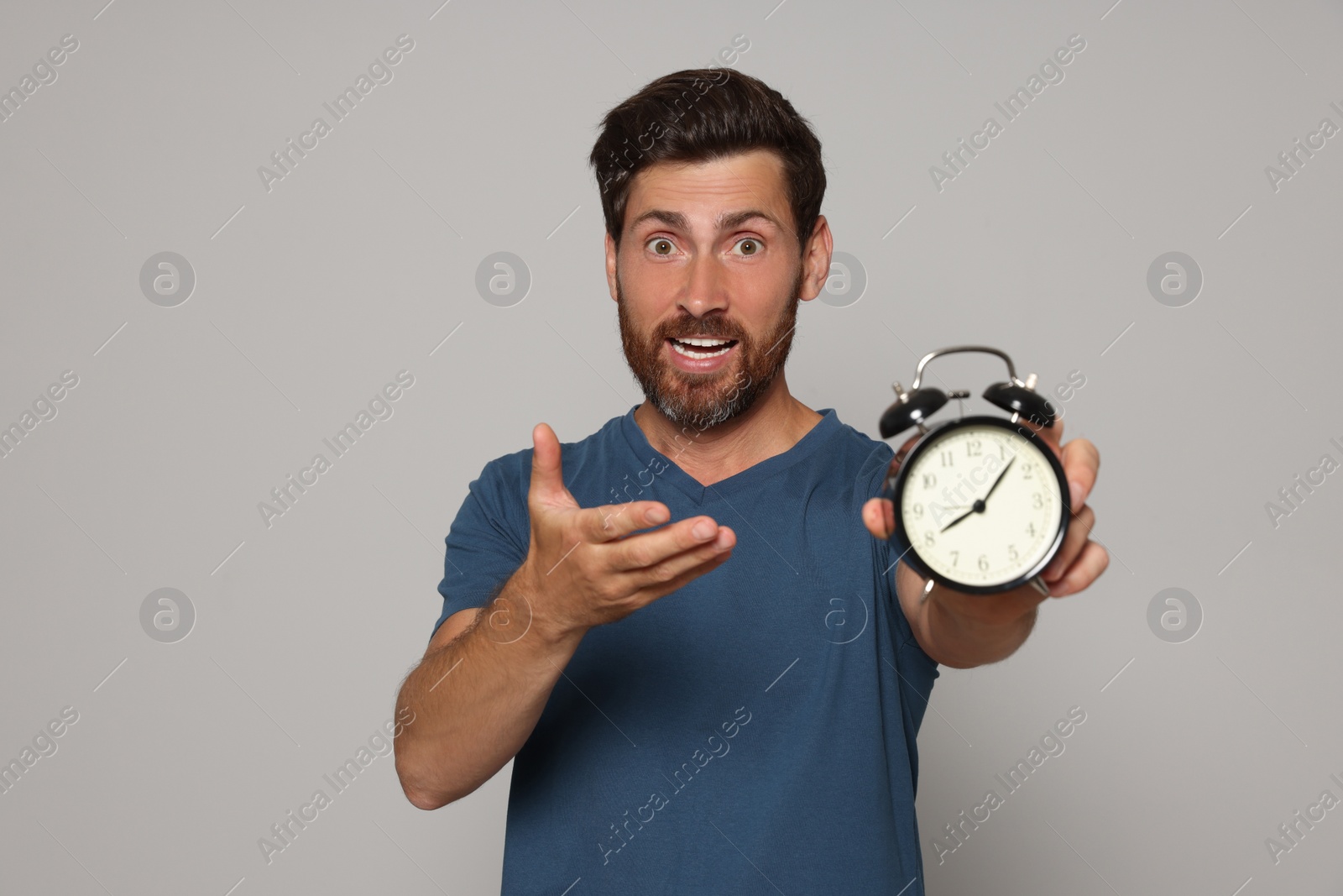 Photo of Emotional bearded man with alarm clock on light grey background. Being late concept