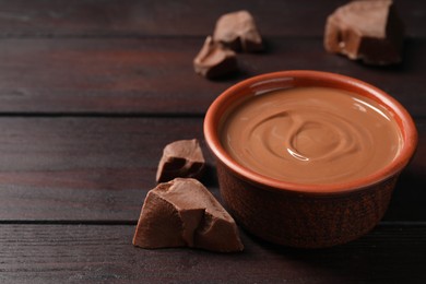 Photo of Tasty milk chocolate paste in bowl and pieces on wooden table, closeup. Space for text