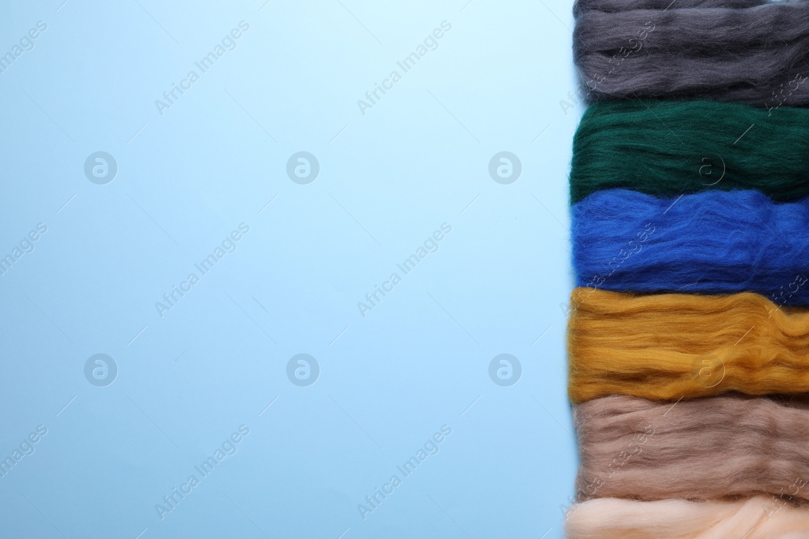 Photo of Colorful felting wool on light blue background, flat lay. Space for text