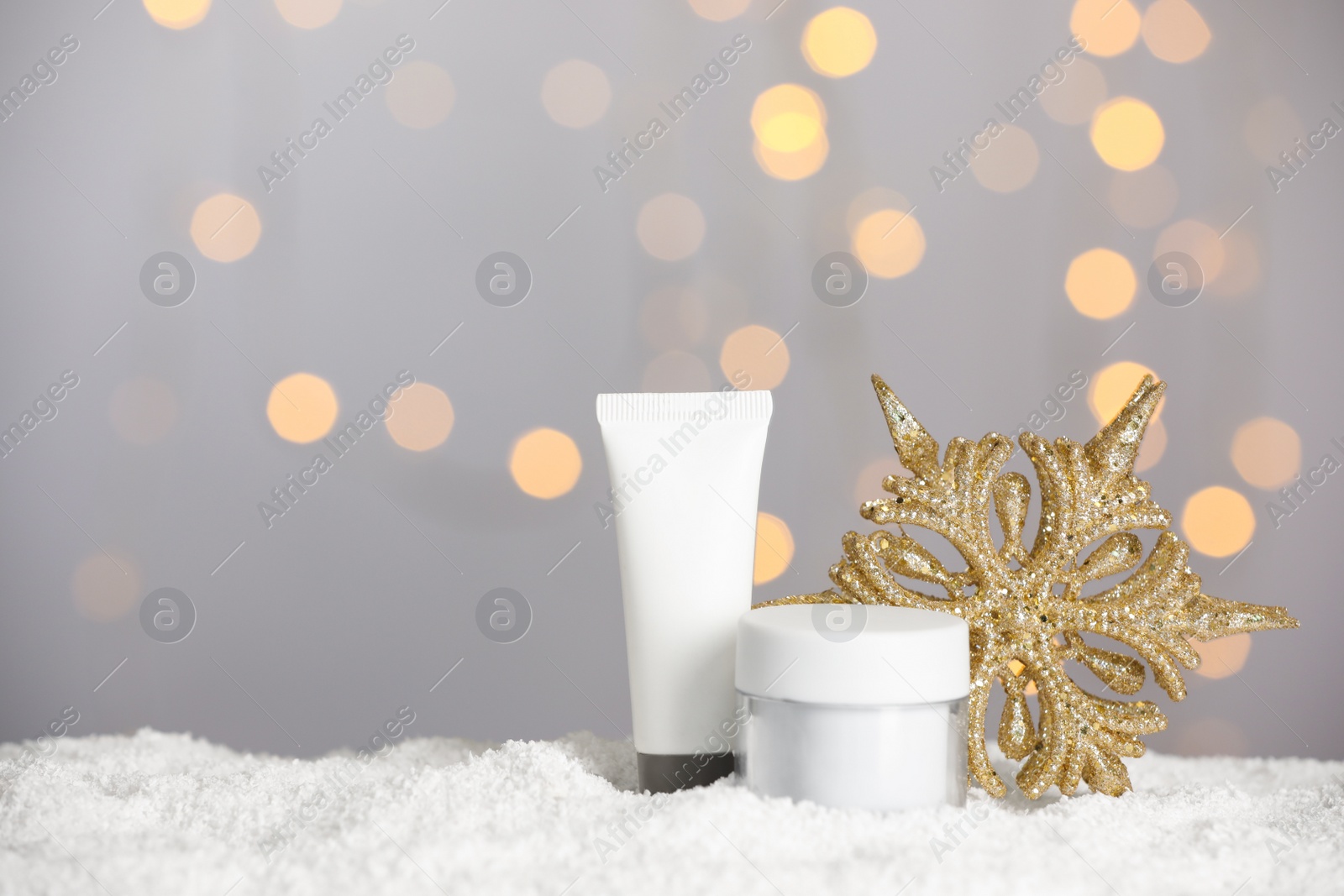 Photo of Set of winter skin care cosmetics with hand cream and decorative snowflake on snow against blurred lights. Space for text