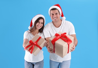 Photo of Beautiful happy couple in Santa hats holding Christmas gifts on light blue background