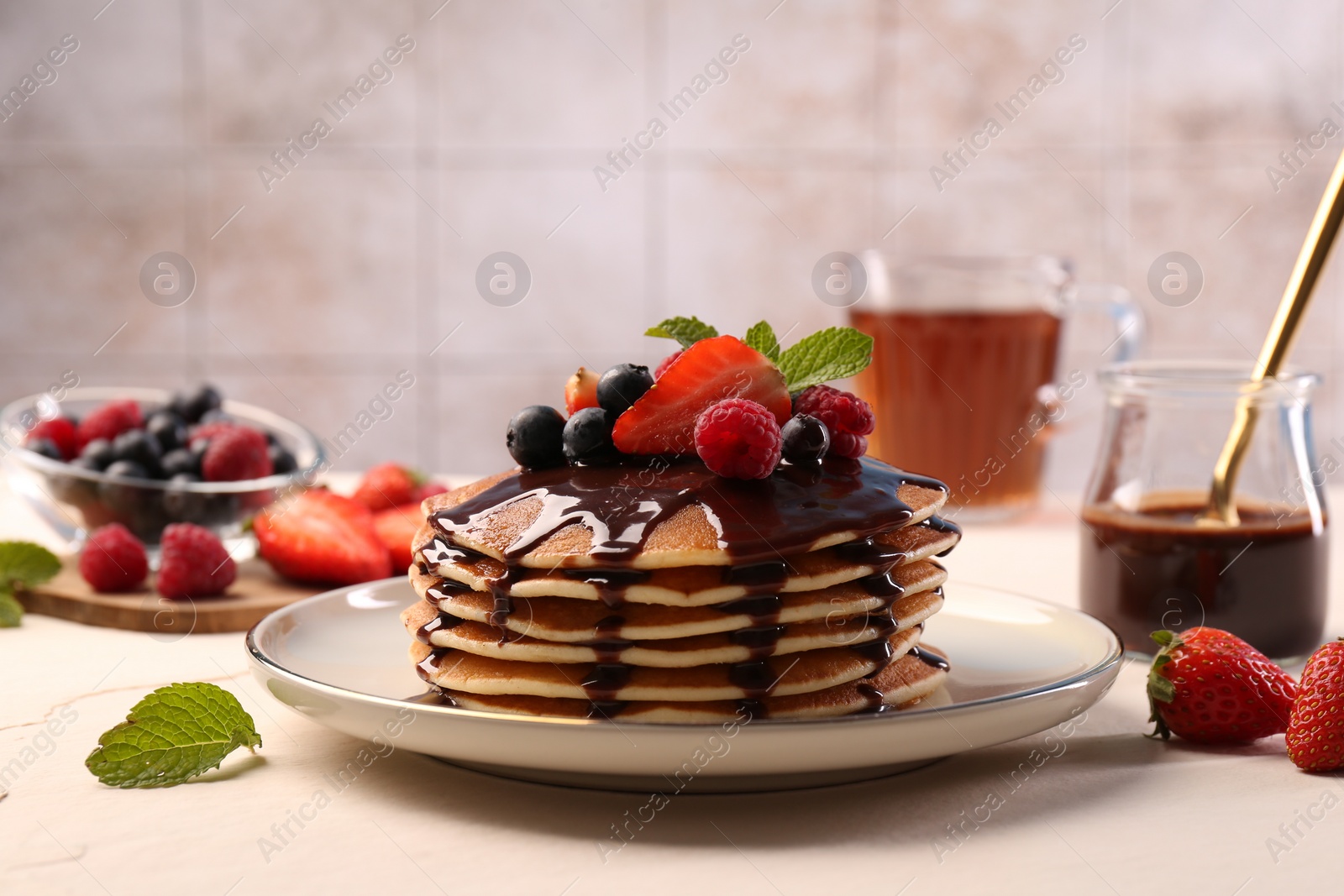Photo of Stack of tasty pancakes with fresh berries, chocolate sauce and mint on white table
