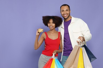 Photo of Happy African American couple with shopping bags and credit card on purple background. Space for text