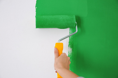 Photo of Woman painting white wall with green dye, closeup. Interior renovation