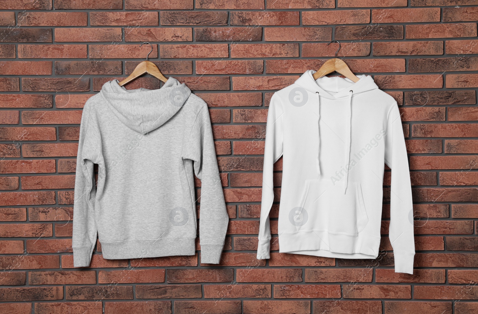 Photo of Hangers with new sweaters on brick wall, mock up for design