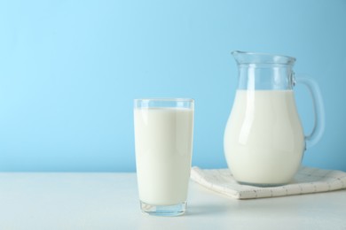 Photo of Jug and glass of fresh milk on white table against light blue background