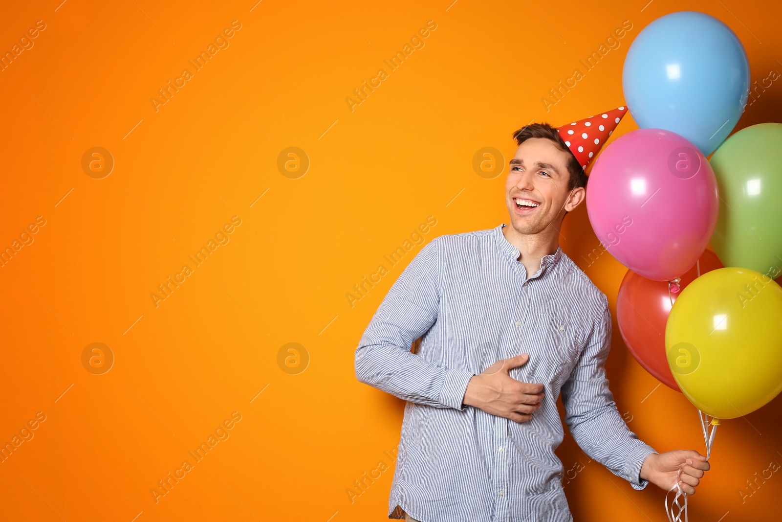 Photo of Young man with bright balloons on color background. Birthday celebration