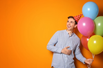 Young man with bright balloons on color background. Birthday celebration