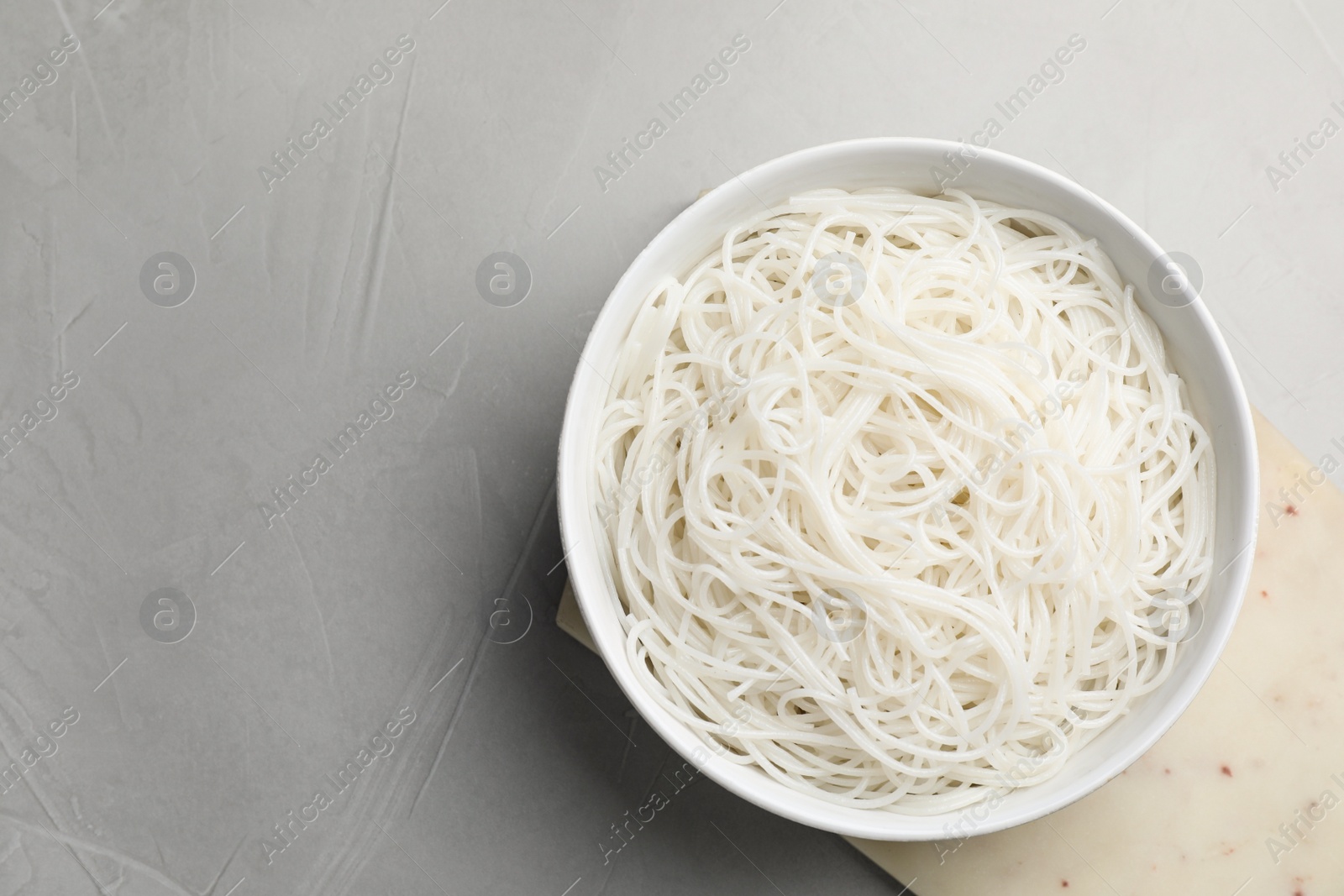 Photo of Bowl with cooked rice noodles on light grey table, top view. Space for text