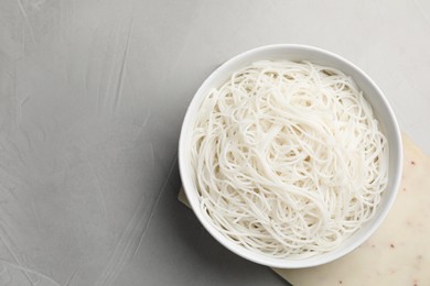 Bowl with cooked rice noodles on light grey table, top view. Space for text