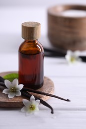 Photo of Vanilla pods, flowers and bottle with essential oil on white wooden table, closeup