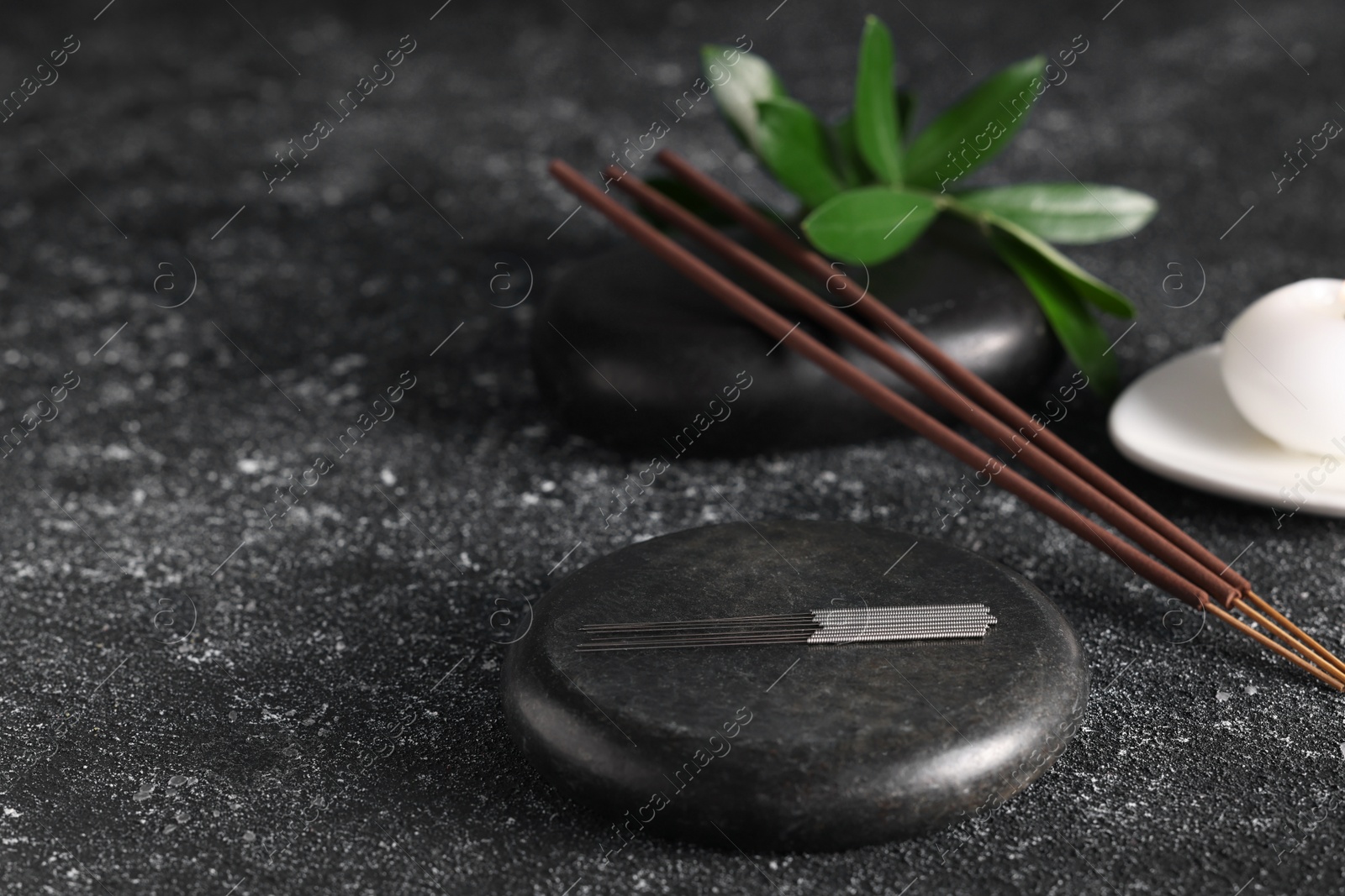 Photo of Acupuncture needles, spa stones and aromatic incense sticks on black textured table. Space for text