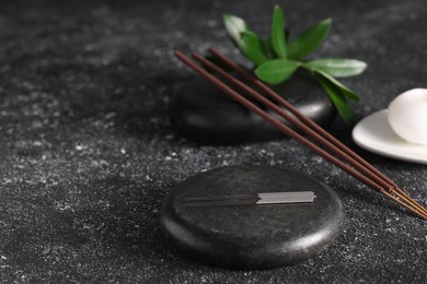 Photo of Acupuncture needles, spa stones and aromatic incense sticks on black textured table. Space for text