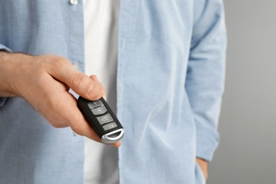 Young man holding car smart key on grey background, closeup