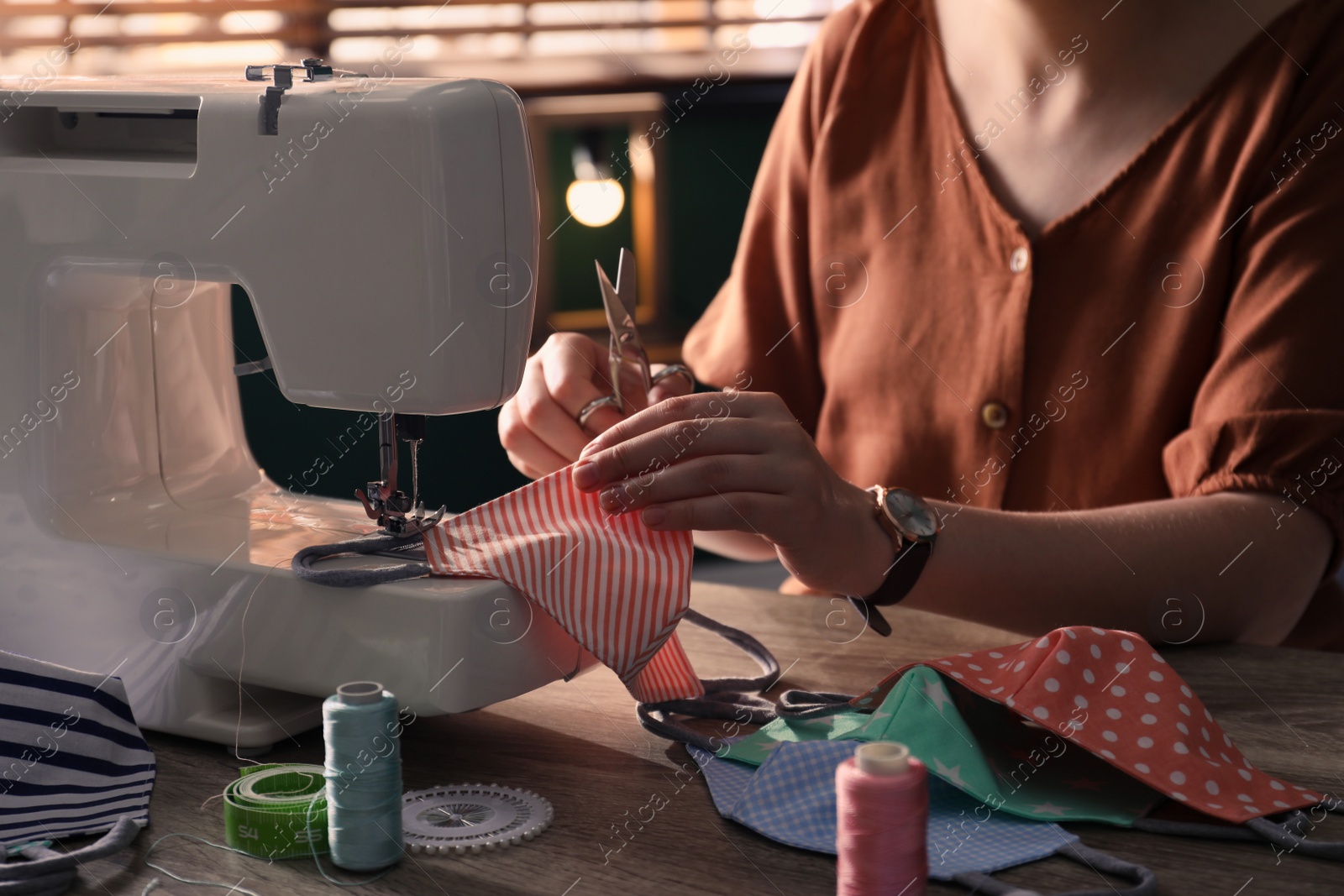 Photo of Woman sewing cloth protective mask with machine at table indoors, closeup