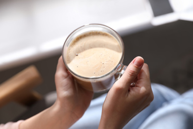 Woman with cup of coffee indoors, closeup