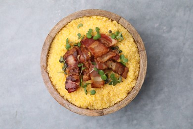 Photo of Cooked cornmeal with bacon and microgreens in bowl on light grey table, top view