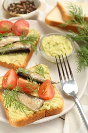Photo of Delicious sandwiches with sprats, tomatoes, dill and avocado puree served on white wooden table
