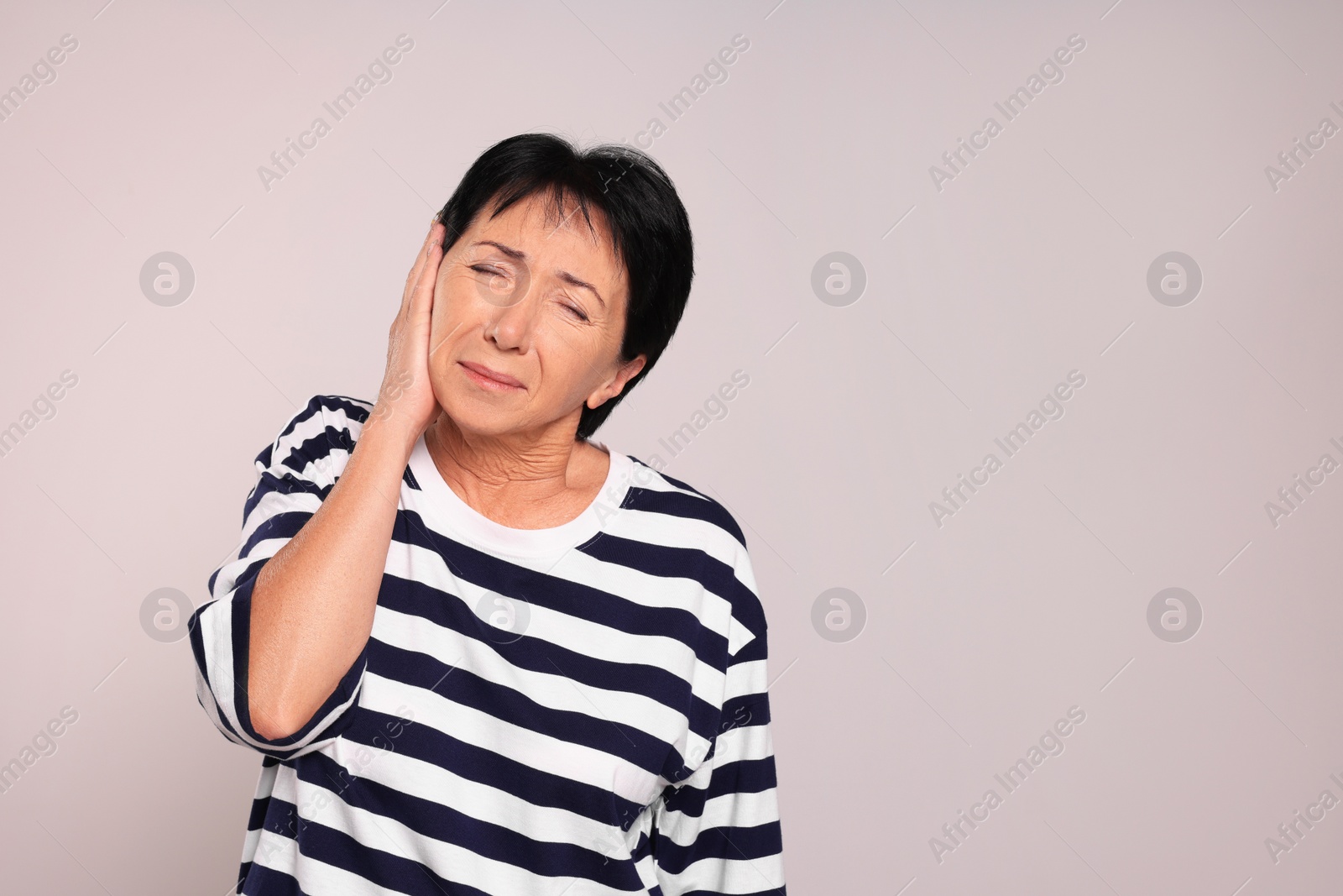 Photo of Senior woman suffering from ear pain on light grey background. Space for text