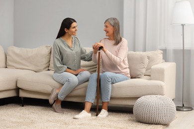 Mature lady with walking cane and young woman on sofa at home