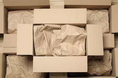 Photo of Many open cardboard boxes with crumpled paper on wooden floor, flat lay