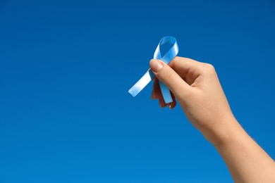 Photo of Woman holding light blue awareness ribbon against sky, closeup