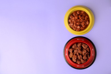Photo of Wet pet food in feeding bowls on violet background, flat lay. Space for text