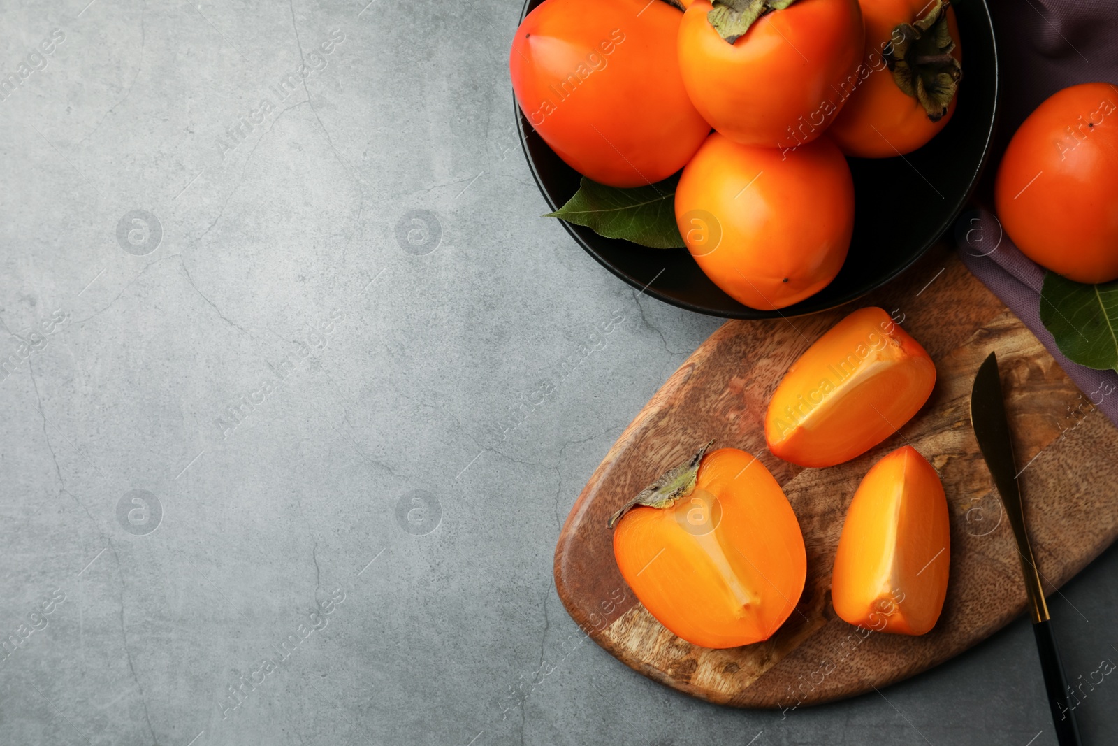 Photo of Delicious ripe persimmons and knife on light gray textured table, flat lay. Space for text