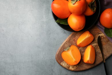 Photo of Delicious ripe persimmons and knife on light gray textured table, flat lay. Space for text