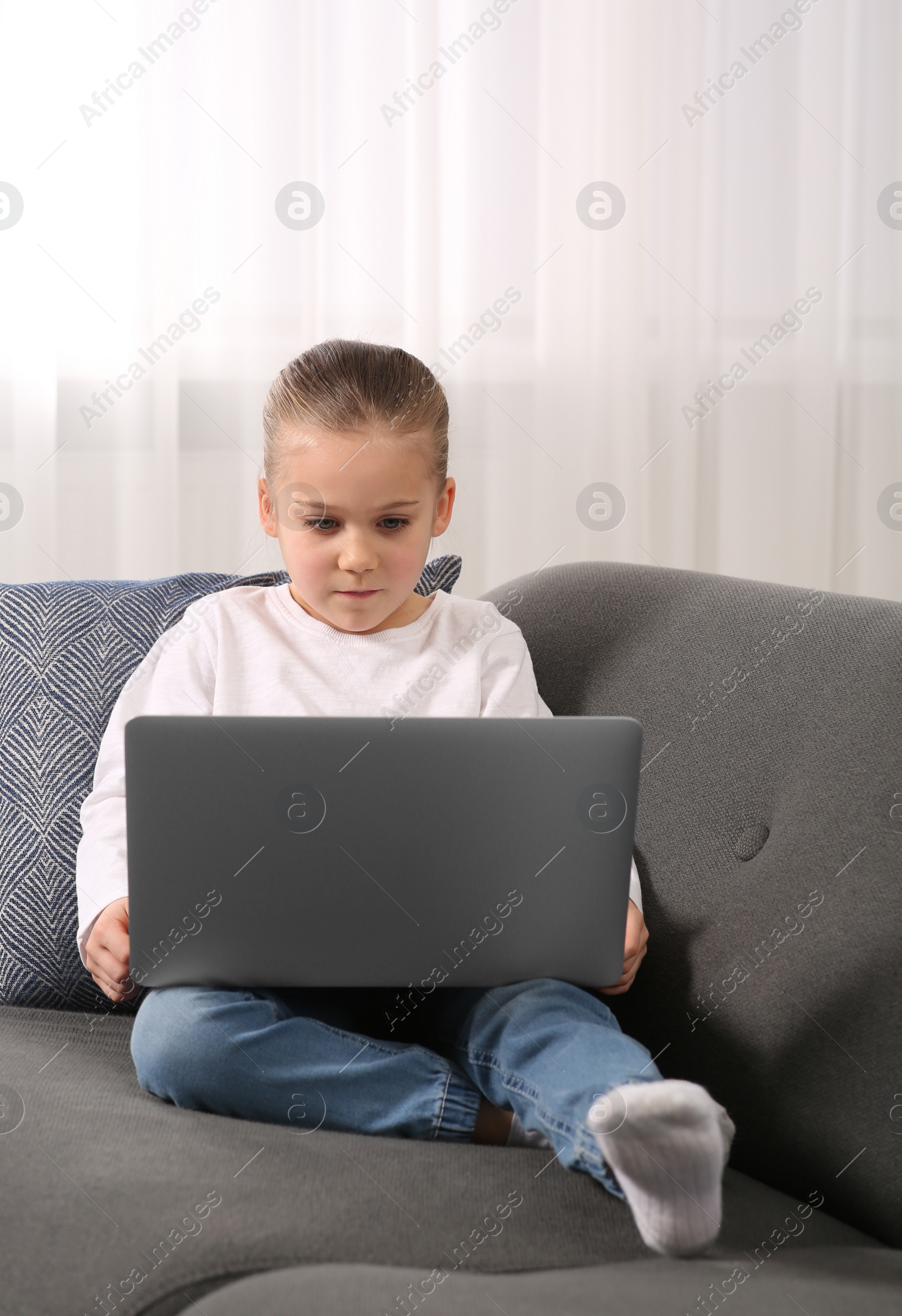 Photo of Little girl using laptop on sofa at home. Internet addiction