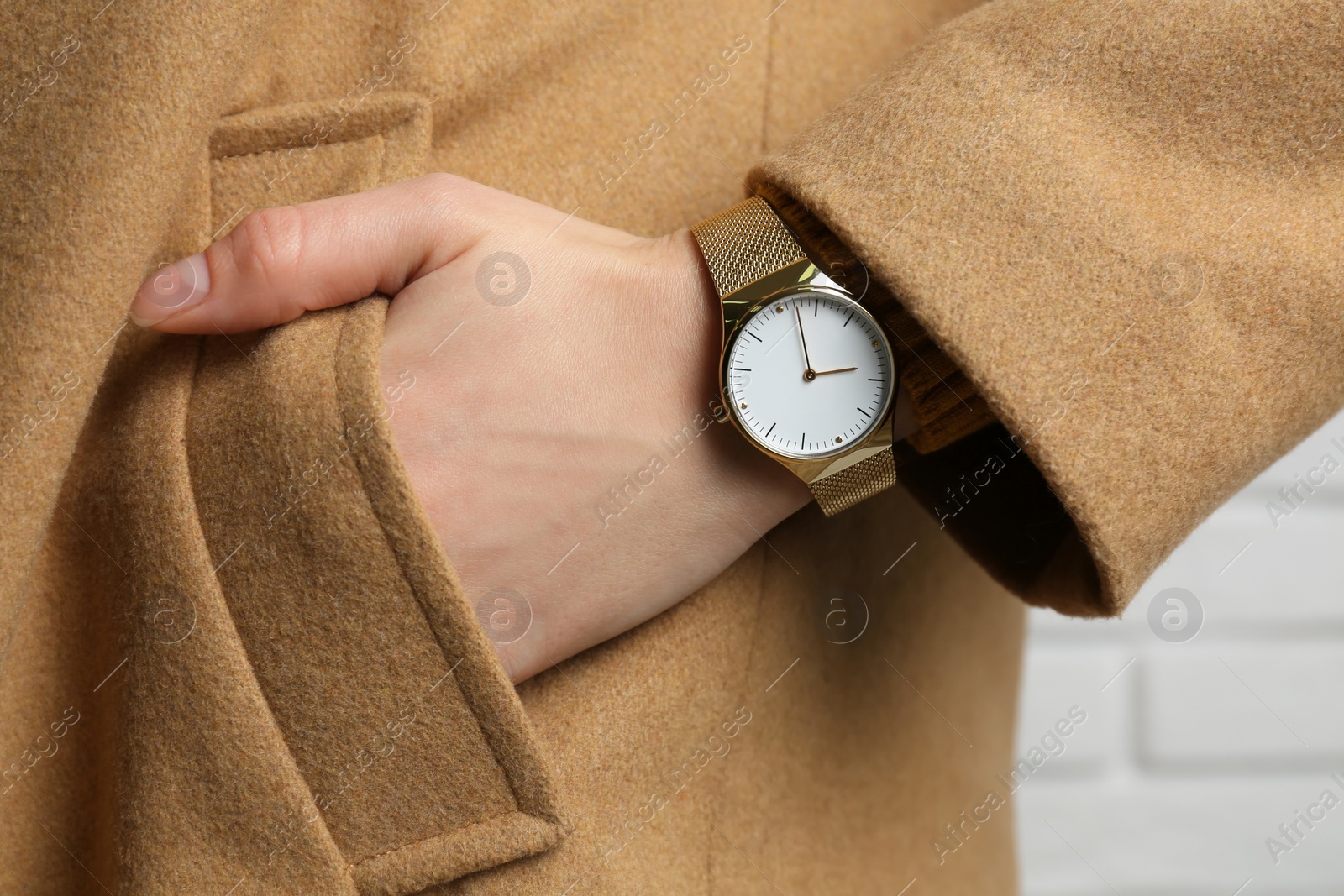 Photo of Woman wearing luxury wristwatch near white brick wall, closeup