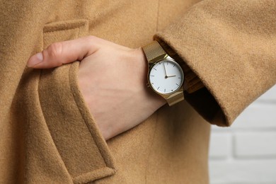 Woman wearing luxury wristwatch near white brick wall, closeup