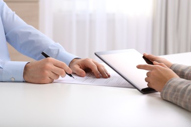 Photo of Businesspeople signing contract at white table in office, closeup of hands