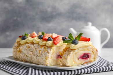 Photo of Tasty meringue roll with jam, cream, strawberry, blueberry and mint on table, closeup
