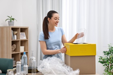 Photo of Garbage sorting. Smiling woman throwing plastic container into cardboard box in room