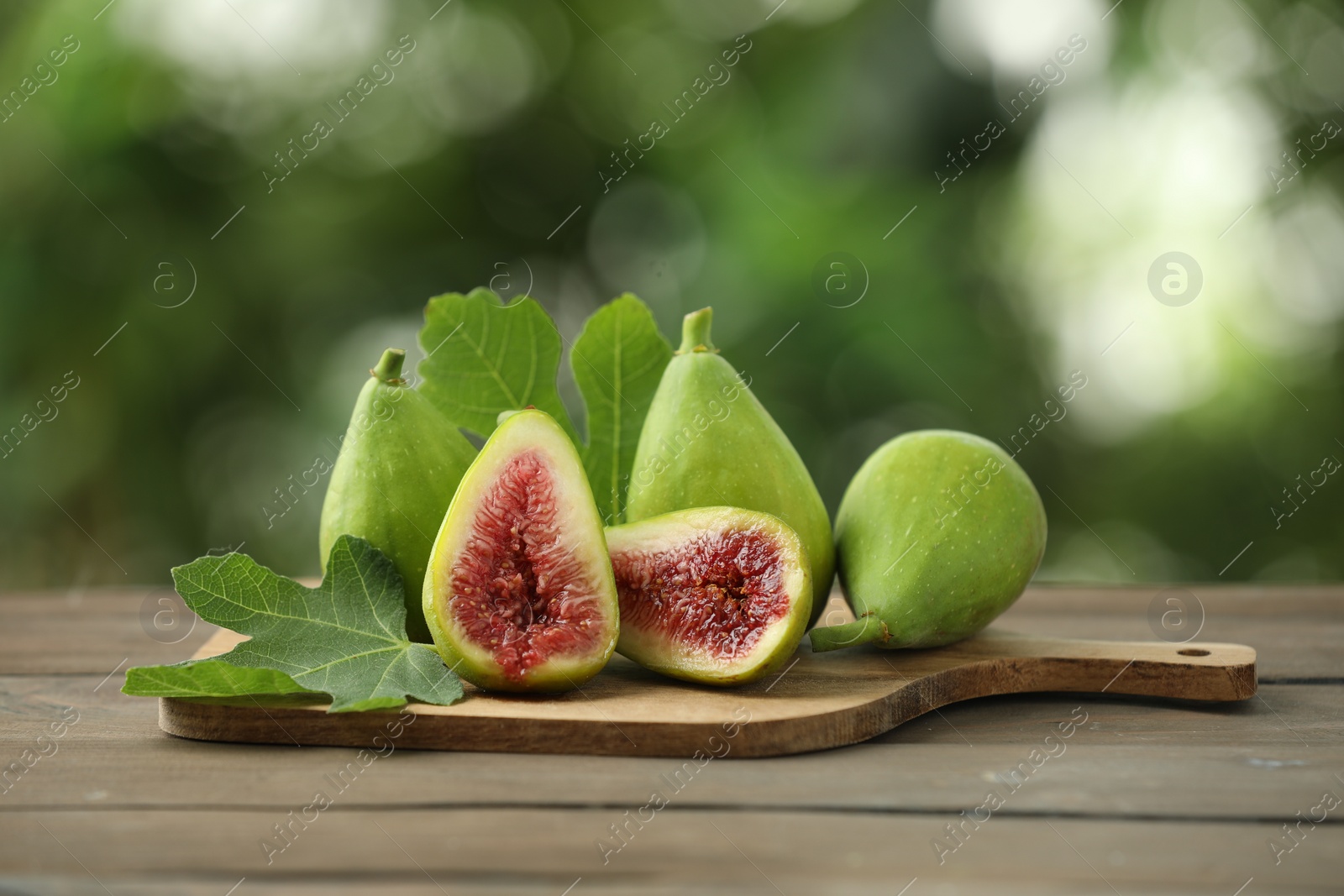 Photo of Cut and whole green figs on wooden table against blurred background