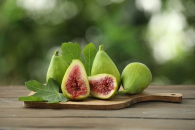 Photo of Cut and whole green figs on wooden table against blurred background