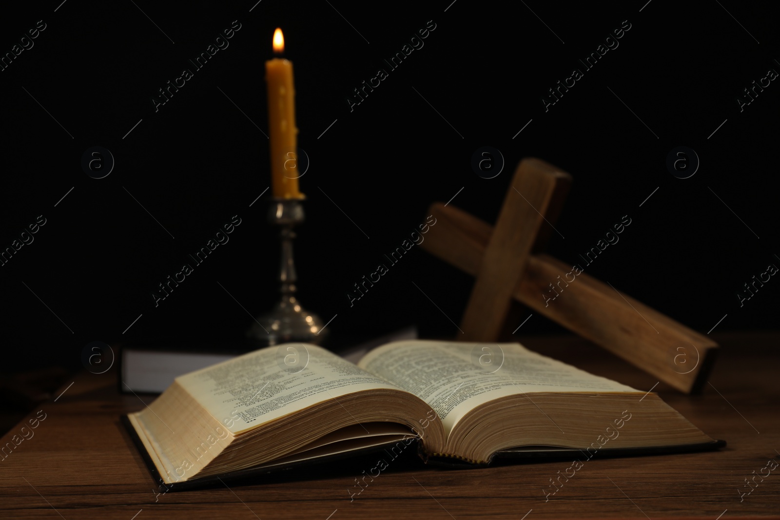 Photo of Church candle, Bible and cross on wooden table against black background