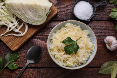 Bowl of tasty sauerkraut and ingredients on wooden table, flat lay