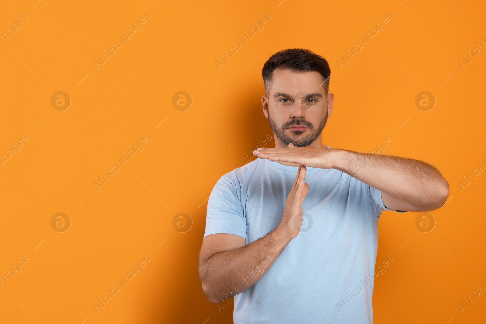 Photo of Handsome man showing time out gesture on orange background, space for text. Stop signal